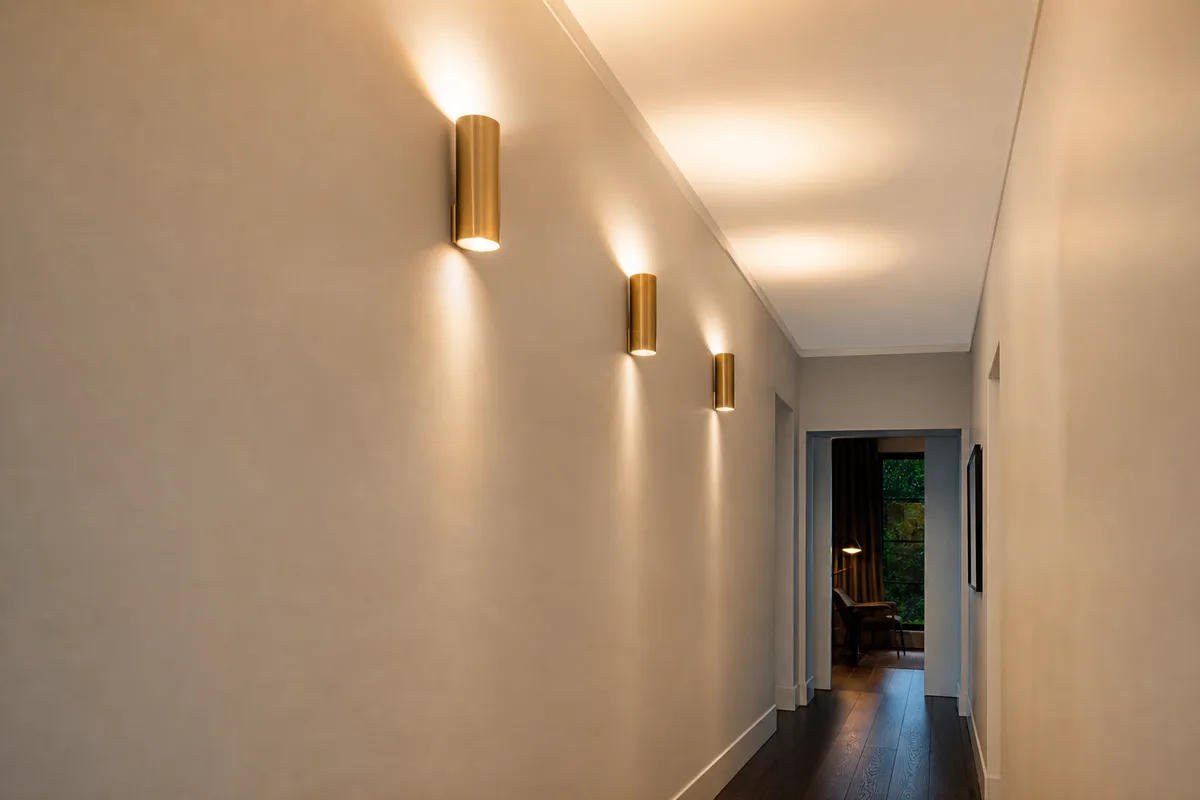 Couloir étroit éclairé par une série d’appliques murales orientées vers le plafond