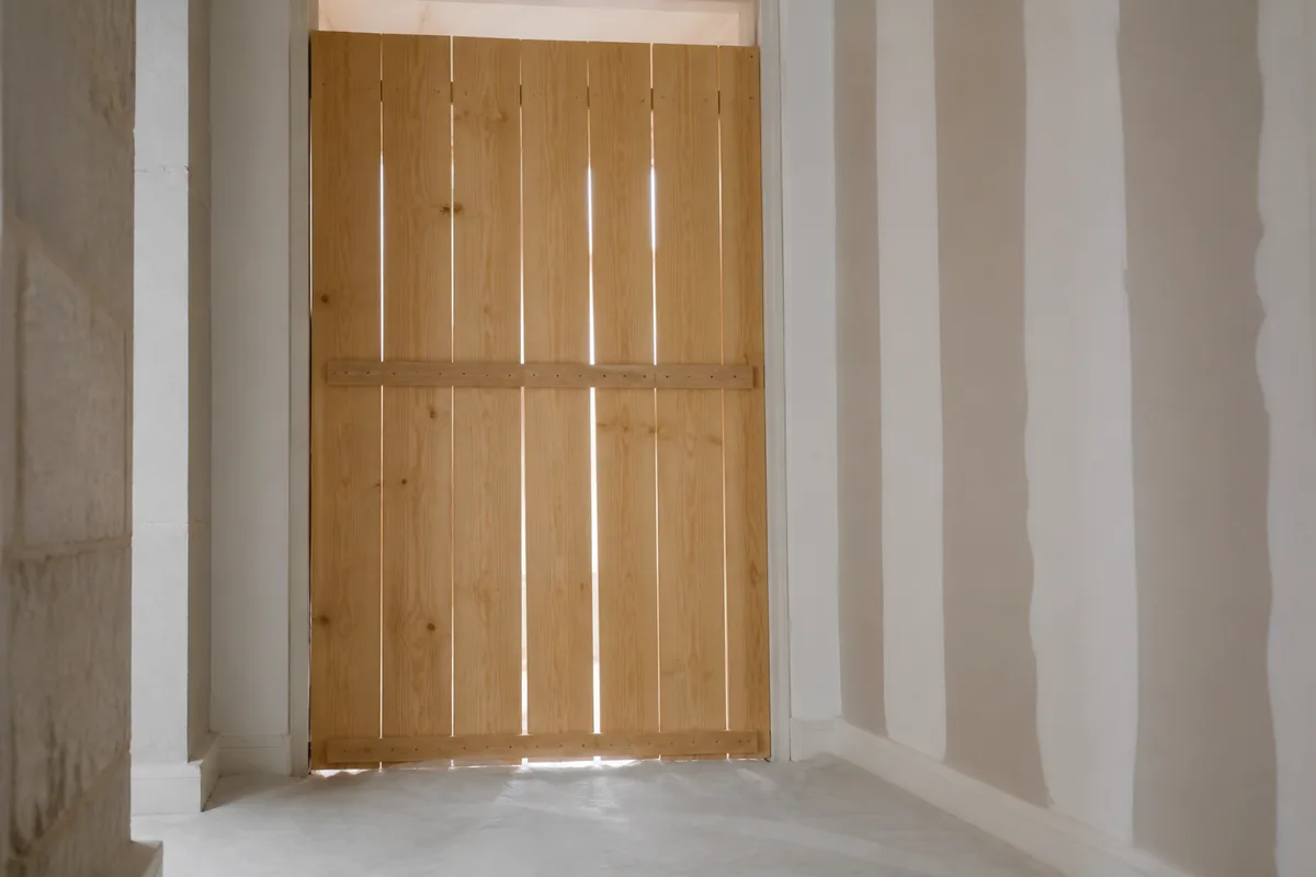 Palissade de bois brut fermant l’accès à une pièce en travaux, sol protégé